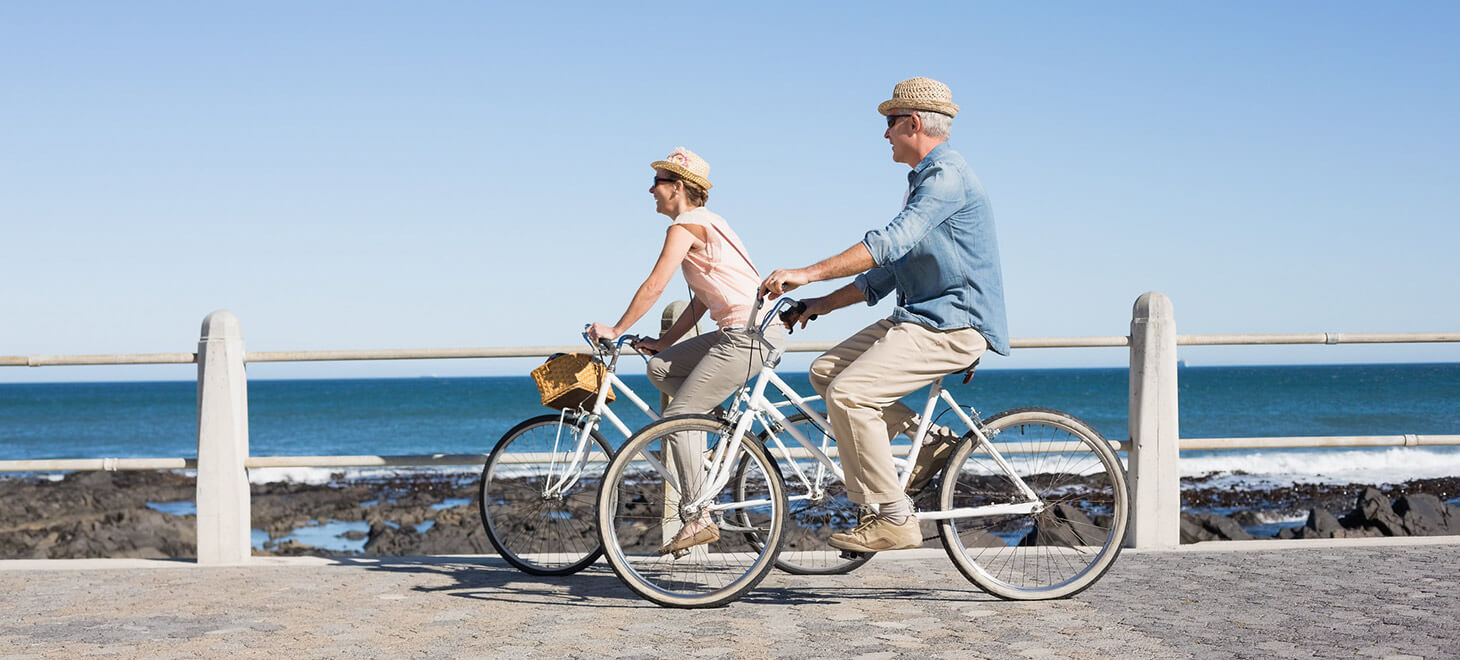 Older couple riding bikes by the ocean enjoy their getaway in Maine